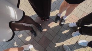 A diverse group of stylish footwear is displayed, including black heels, loafers, and white sneakers, showcasing a variety of trendy designs against a sunlit backdrop.